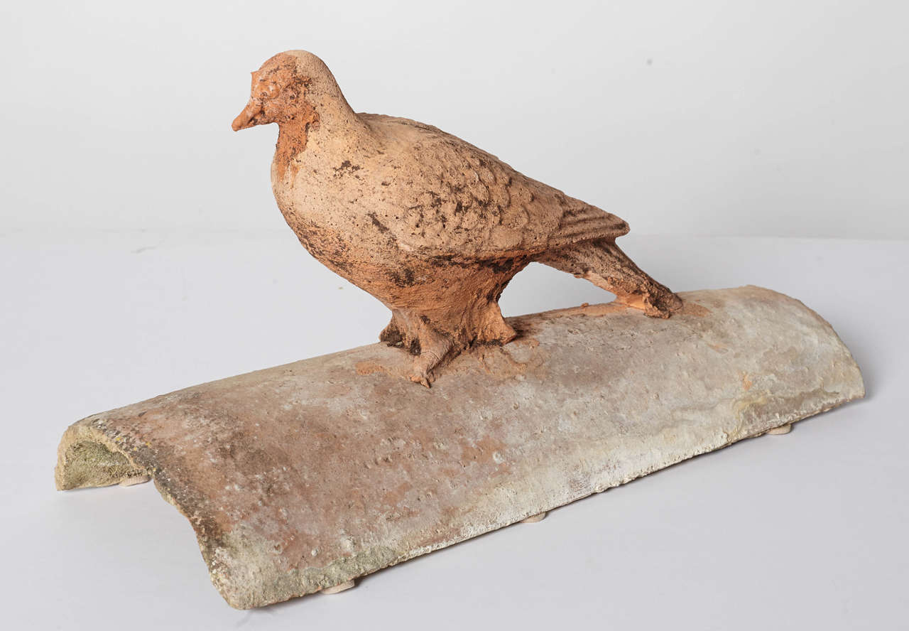Terracotta bird perched on roof tile.